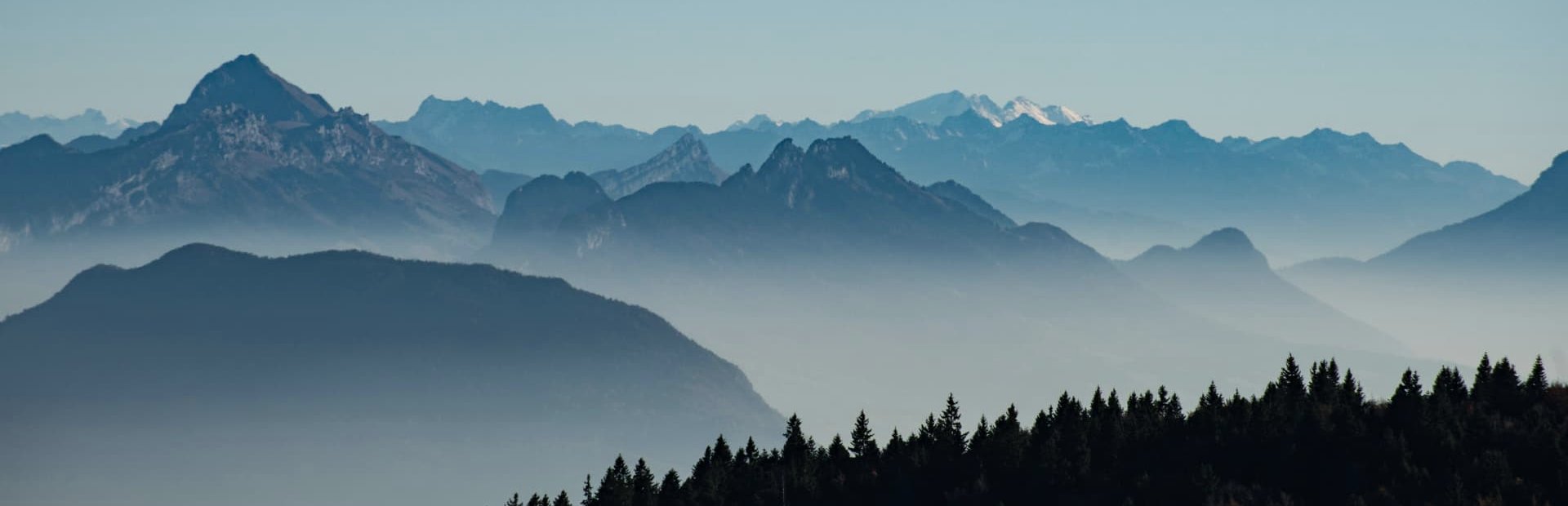 Layered mountain ridges receding into morning mist above a dark treeline